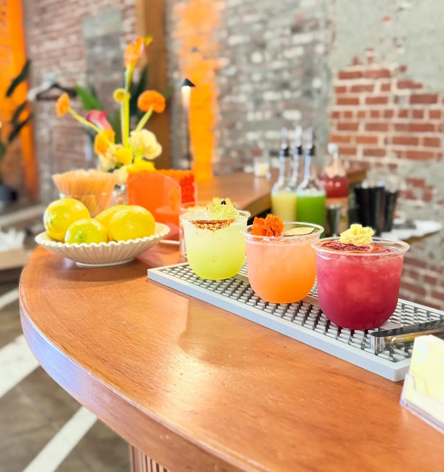 Colourful cocktails and a bowl of citrus on a wooden bar against a brick wall