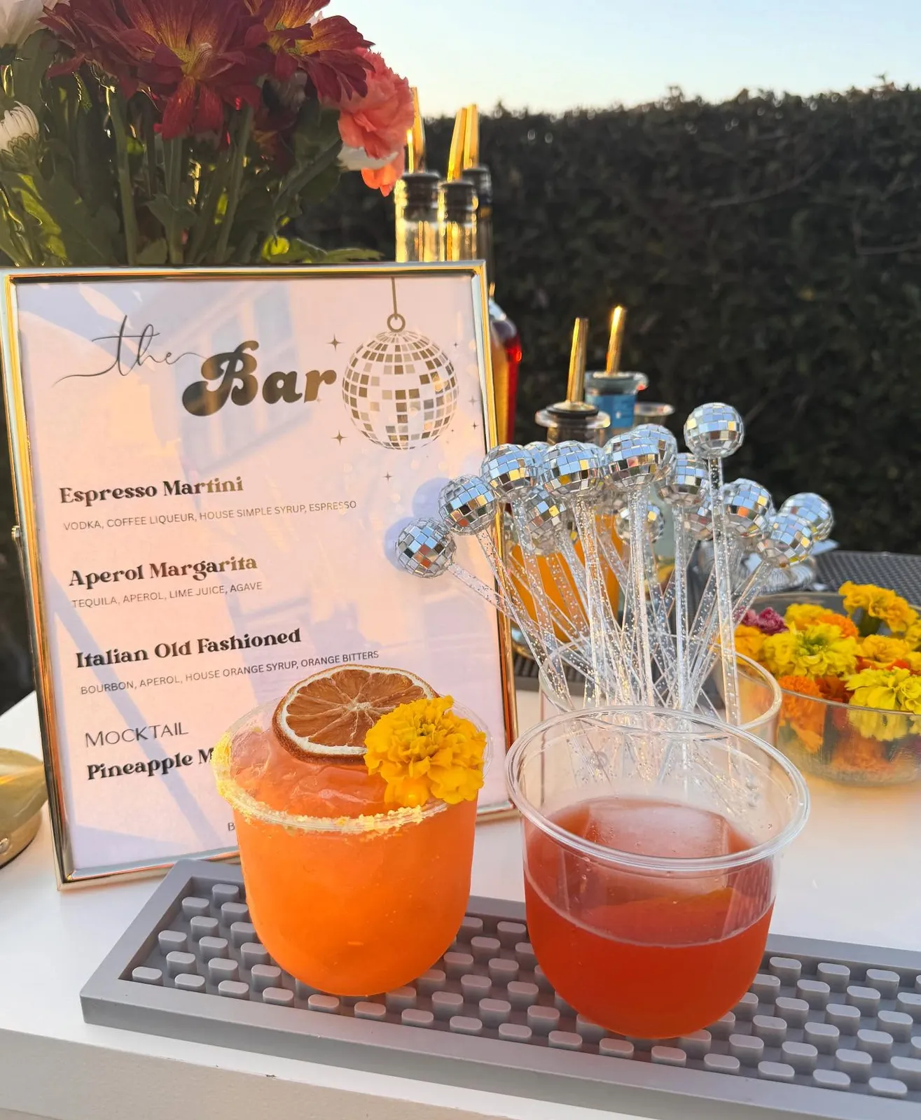 A bar menu with disco ball stirrers and orange cocktails at golden hour