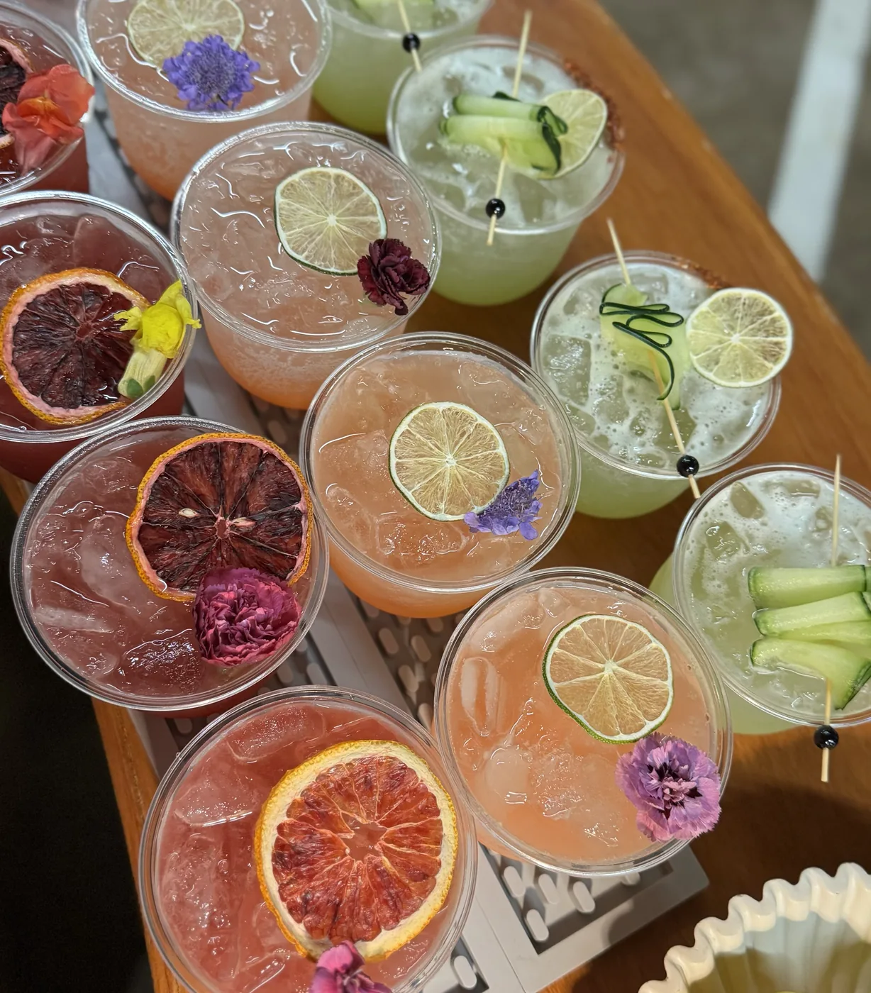 An overhead row of cocktails garnished with cucumber ribbons, dried citrus and edible flowers