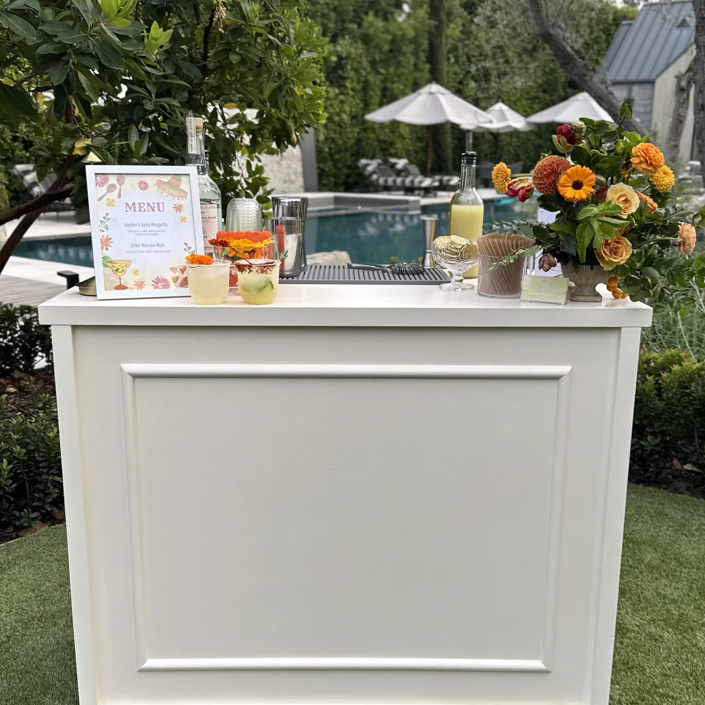 The With A Twist mobile bar set up beside a pool, styled with a printed menu and autumn florals